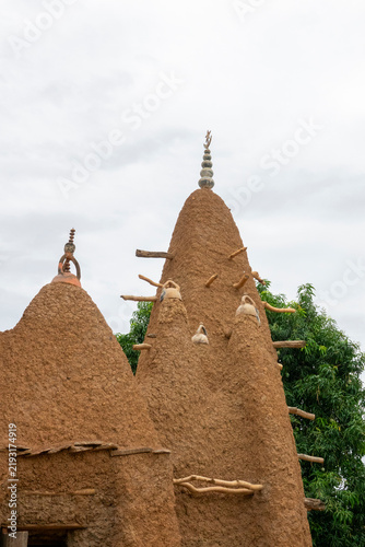 Wooden support pegs jut from two mud towers of the 17th-century Sudano-Sahelian mosque beside a mango tree, Savanes district, Kouto, Ivory Coast