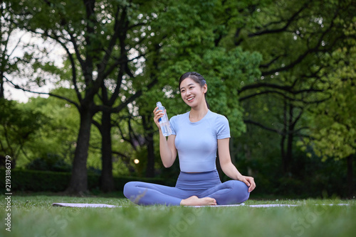 Quadro su tela Smiling woman holding water bottle while sitting on yoga mat in park