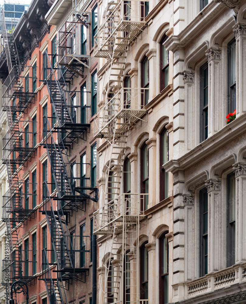Obraz premium Historic brick facades of classic buildings with exterior iron fire escapes located in the iconic SoHo neighborhood in Manhattan, New York, displaying traditional urban architecture.