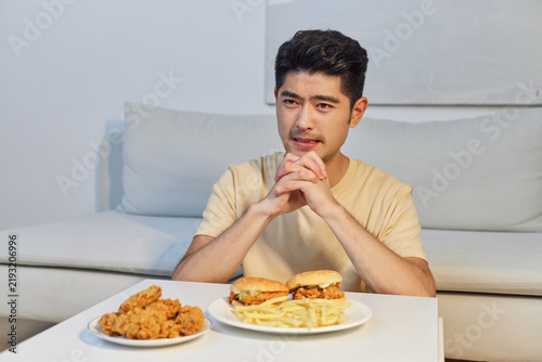 Fotografie Thoughtful young man looking at a large fast food meal at home