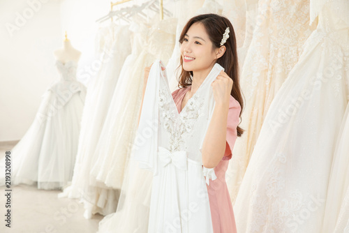Happy Asian bride choosing a white wedding dress in a bridal shop