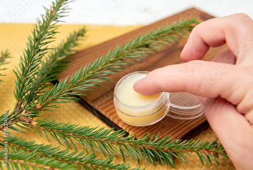 Picea abies, Norway spruce herbal medicinal resin lotion in a jar. Used in traditional medicine and the beauty industry. Close-up of a woman’s finger taking spruce tree salve.