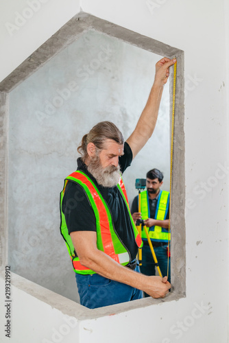 Construction worker measuring window opening with tape measure at house building site