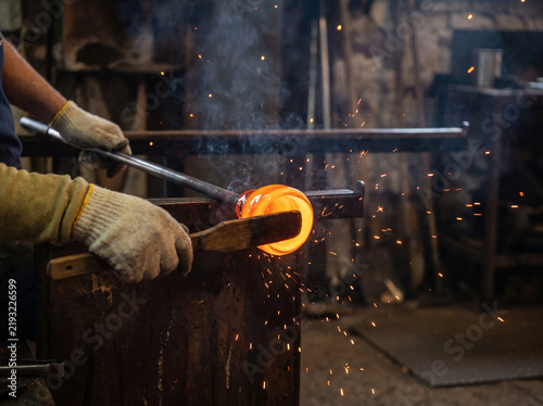 Traditional Glassblower Hands Shaping Molten Glowing Glass with Blowpipe in Workshop