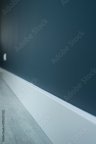 A freshly painted wall in a storm-grey shade with a clean white baseboard, showcasing modern interior finishing and color contrast. 