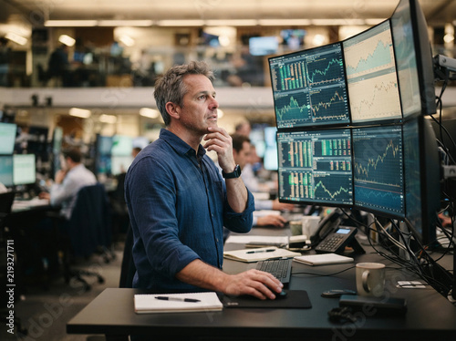 Man with a hand on his chin in thought at an open plan office work desk