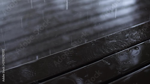 Rain falling onto a wet wooden surface, creating ripples and splashes.