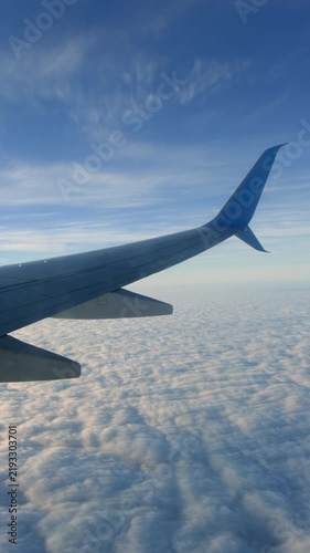 Airplane wing flying above veil of clouds in blue sky with sunlight, vertical video