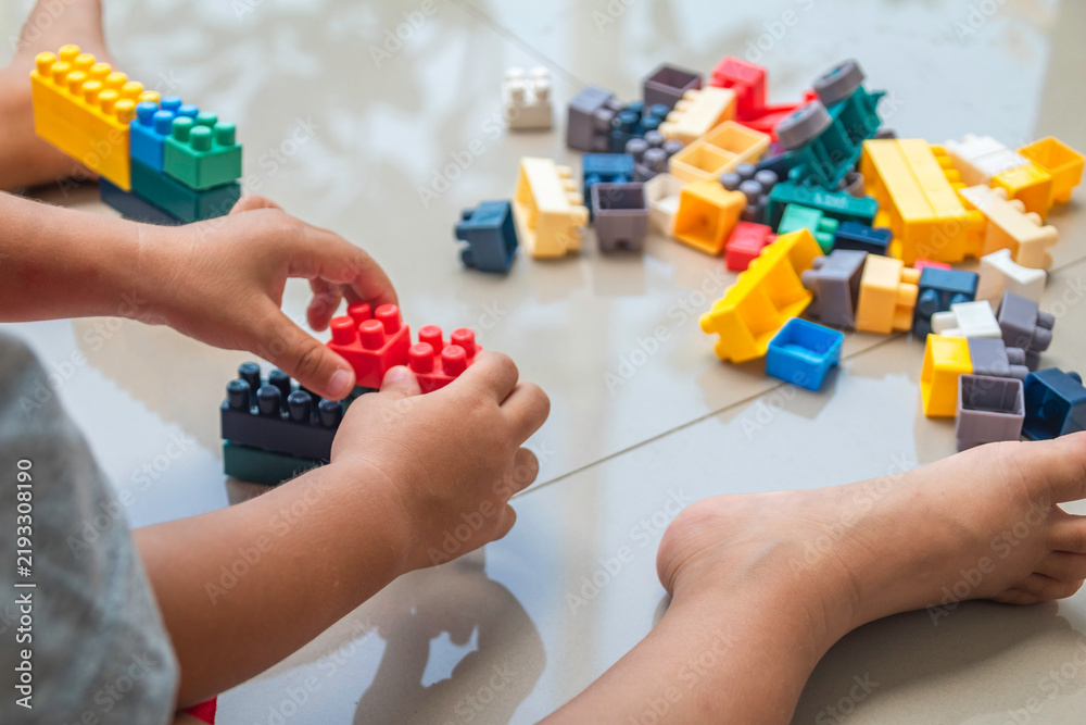 Obraz premium Kids' hands assembling colorful toy building blocks indoors, illustrating early childhood education, learning, and creative play concepts.
