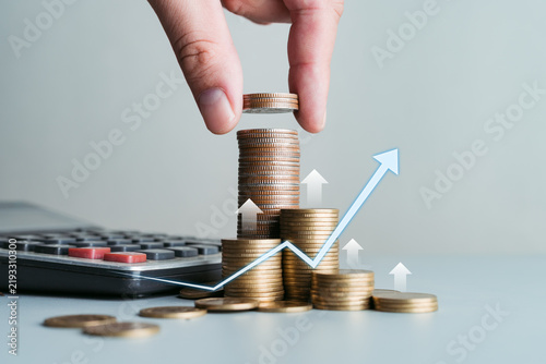 Hand Placing Coin on Stacks with Upward Growth Arrows and Calculator, representing Financial Growth, Investment, and Profit Concept