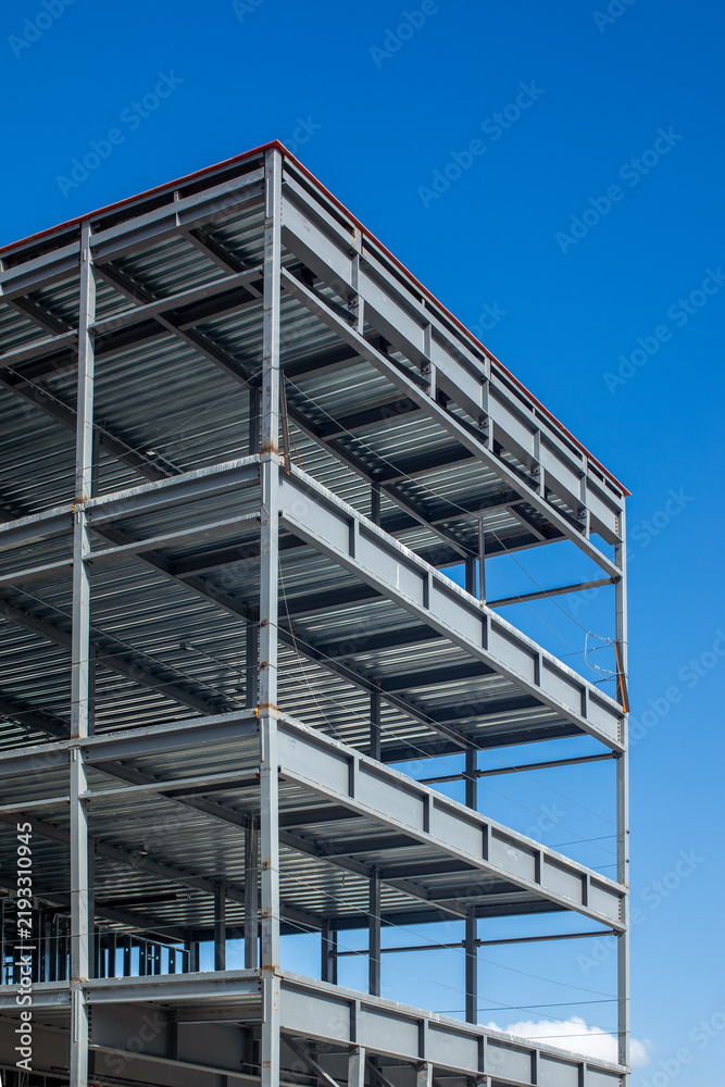 Fototapeta premium Multi story structural steel frame building under construction against a clear blue sky