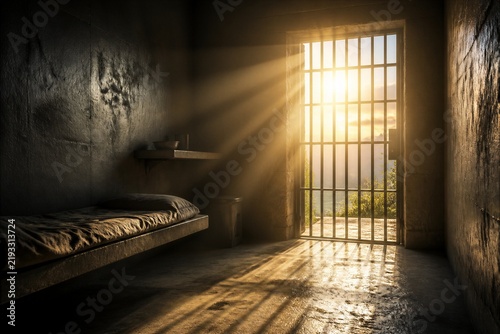 Prison cell illuminated by sunlight through barred door
