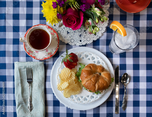High angle view of elegant picnic style lunch with chicken salad sandwich, chips, and tea on a checkered tablecloth.