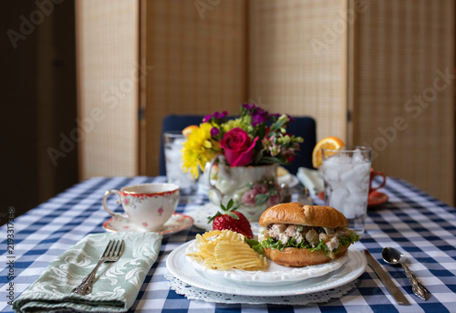 elegant picnic style lunch with chicken salad sandwich, chips, and tea on a checkered tablecloth.