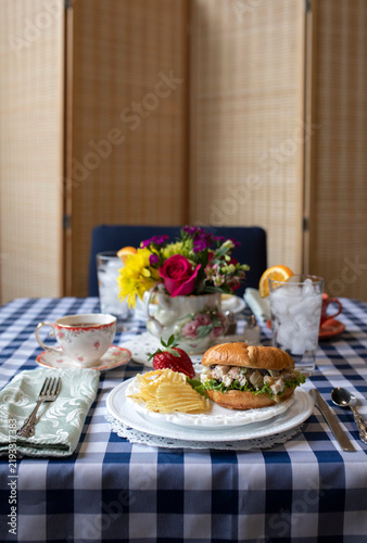 elegant picnic style lunch with chicken salad sandwich, chips, and tea on a checkered tablecloth.