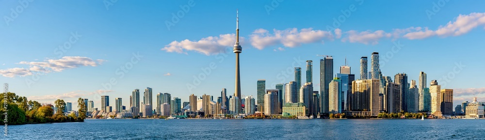 Obraz premium Panoramic View of a Modern City Skyline with Tall Buildings and a Tower Overlooking a Calm Body of Water Under a Blue Sky