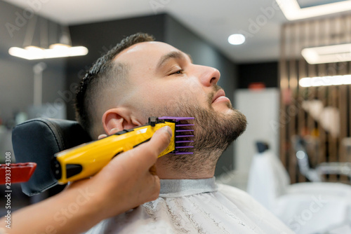 Barber trim beard with electric clipper in barbershop