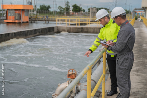 Obraz na plátně Engineer and technician inspect a wastewater treatment basin and record operational data beside industrial pipelines