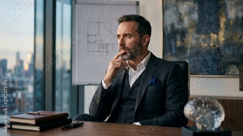 Businessman deep in thought at his desk, modern office, city view