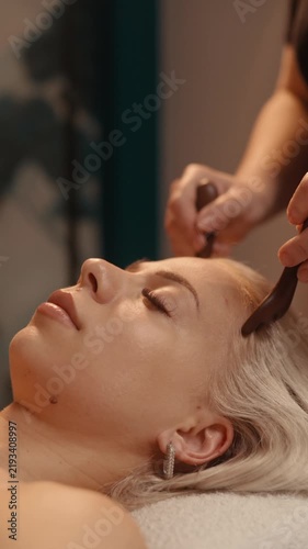 Woman receiving relaxing scalp massage with special comb tool at spa salon, improving blood circulation and promoting hair and wellness care