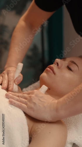 Massagist doing relaxing hot compress massage with herbal sacks. Woman enjoying calming sensual bodycare treatment in spa resort.