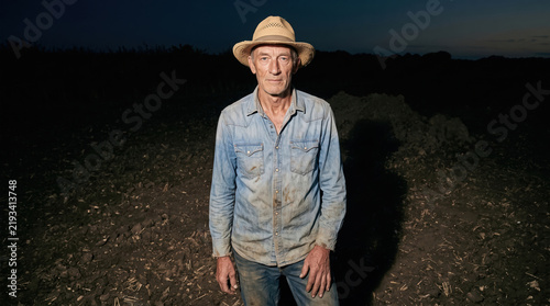 Farmer standing in a field at dusk wearing a straw hat
