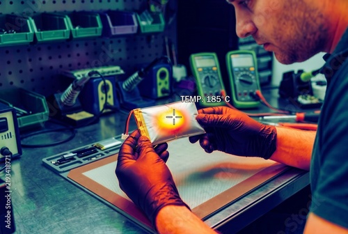 Technician in workshop inspecting a swollen overheating lithium polymer battery using thermal imaging thermography during safety test diagnostics.
