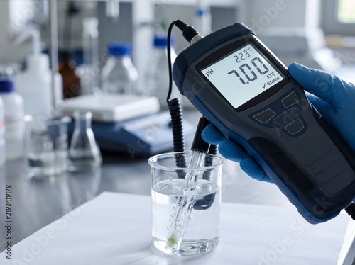 Close-up of a scientist using a digital pH meter with glass electrode probe to measure neutral pH in a liquid beaker within a modern chemical laboratory.