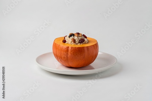 Ghapama on white plate, pumpkin stuffed with rice, nuts, dried cranberries, raisins, providing crunch. Concept of harmony between colors, textures, pumpkin stuffed with rice, nuts, fruit.