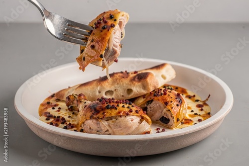 Musakhan on plate, fork lifting savory flatbread with chicken, onions, sumac, pine nuts, drizzled with creamy sauce. Concept of culinary presentation, comfort food appeal.