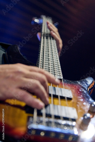 Obraz na plátně Electric bassist plucks strings beneath stage lights in warm wood tones