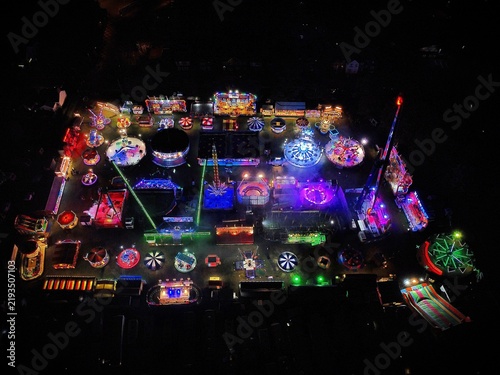 Aerial view of the illuminated funfair at Spencer Park with colorful spinning rides, bright neon lights, and carnival attractions at night in Rushden, England, United Kingdom.
