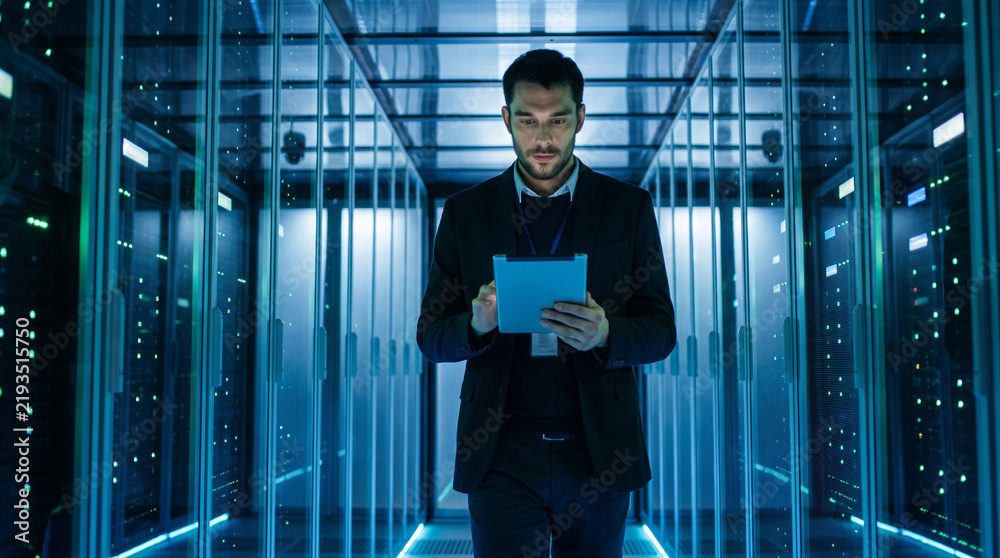 Fototapeta premium Focused professional engineer reviewing tablet device in modern data center environment with intense concentration and serious emotion