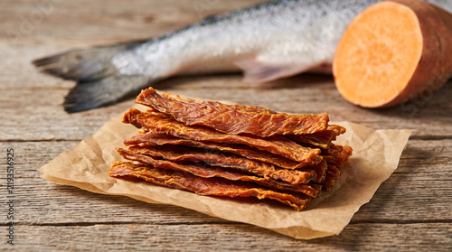  A Rustic Product Photography Layout of All Natural Dehydrated Salmon Jerky Strips for Dogs Piled Neatly Next to Whole Fresh Fish Elements
