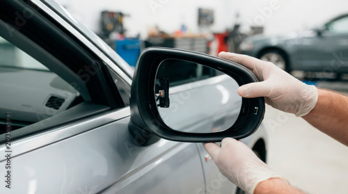 Car repair technician installing side mirror on vehicle in auto service center. Side mirror replacement involves careful handling and precise fitting for optimal view and safety.
