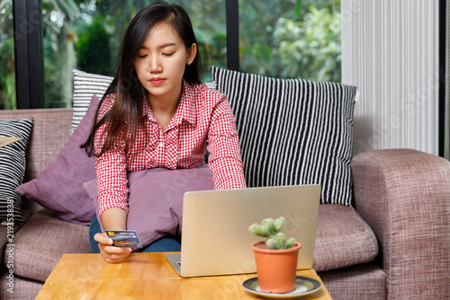 Focused Asian female making internet payment with credit card on laptop. Cyber banking, e-commerce purchase, financial technology, and easy digital lifestyle concept.