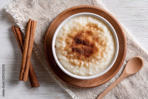 Top view of traditional rice pudding with cinnamon on wooden plate and linen cloth. Great for rustic style family restaurant menu design, cozy autumn recipe blog header or eco grocery web banner