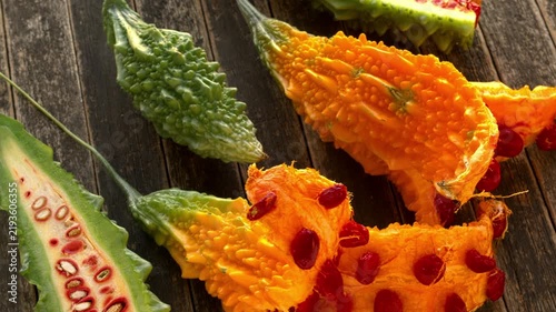 Bitter melons at different stages of ripeness with red seeds on dark, rustic wood. Table spin.