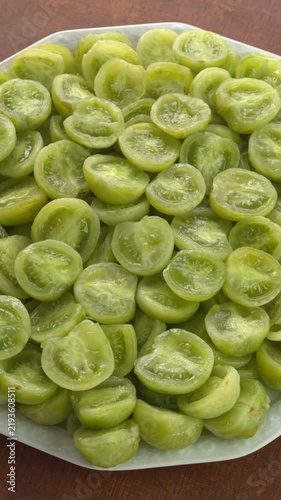 A platter of peeled and halved Green Grape Cherry tomatoes. Ripe organic tomato pieces for homemade jam or another dish, rotating smoothly under natural window light.