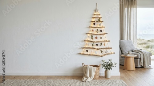 Alternative Christmas tree made of driftwood branches hanging on white wall. Cozy scandinavian living room with armchair, blanket and string lights.