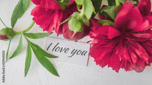 Fotografía Love message on white card surrounded by vivid red flowers and fresh green leave