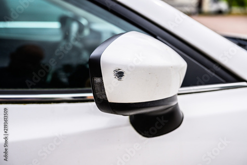 Scratched white car side mirror showing minor collision damage.