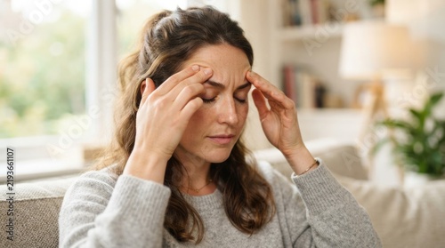 Young Woman Suffering From Headache and Migraine While Sitting at Home and Massaging Her Temples