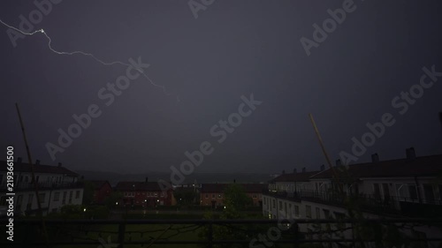 Dramatic lightning bolt illuminating stormy night above residential neighborhood