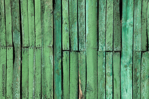 Green fence, backdrop, assembled of pieces. Green surface or covering, faded in the sun, shabby fence (fencing). Wooden boards wall with peeling paint. Green-colored wooden planks texture, background