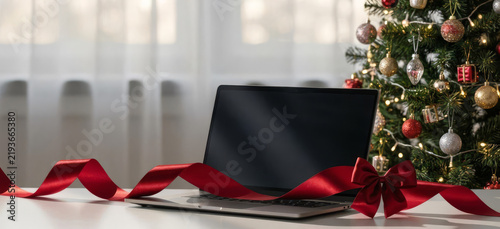 Laptop on table decorated for Christmas with ribbons and a tree  
