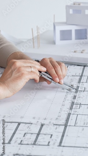 Architect working on a blueprint, using a compass to measure and draw lines for a new building project, creating architectural plans and construction designs with precision