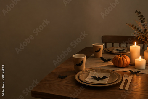 Dining table setting with paper cups, bats, mini pumpkin and candles, Halloween dinner party concept