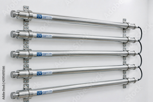 A row of new stainless steel ultraviolet disinfection lamp tubes on a wall.