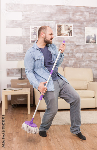 Konstfotografi Man pretending mop is microphone while cleaning at home